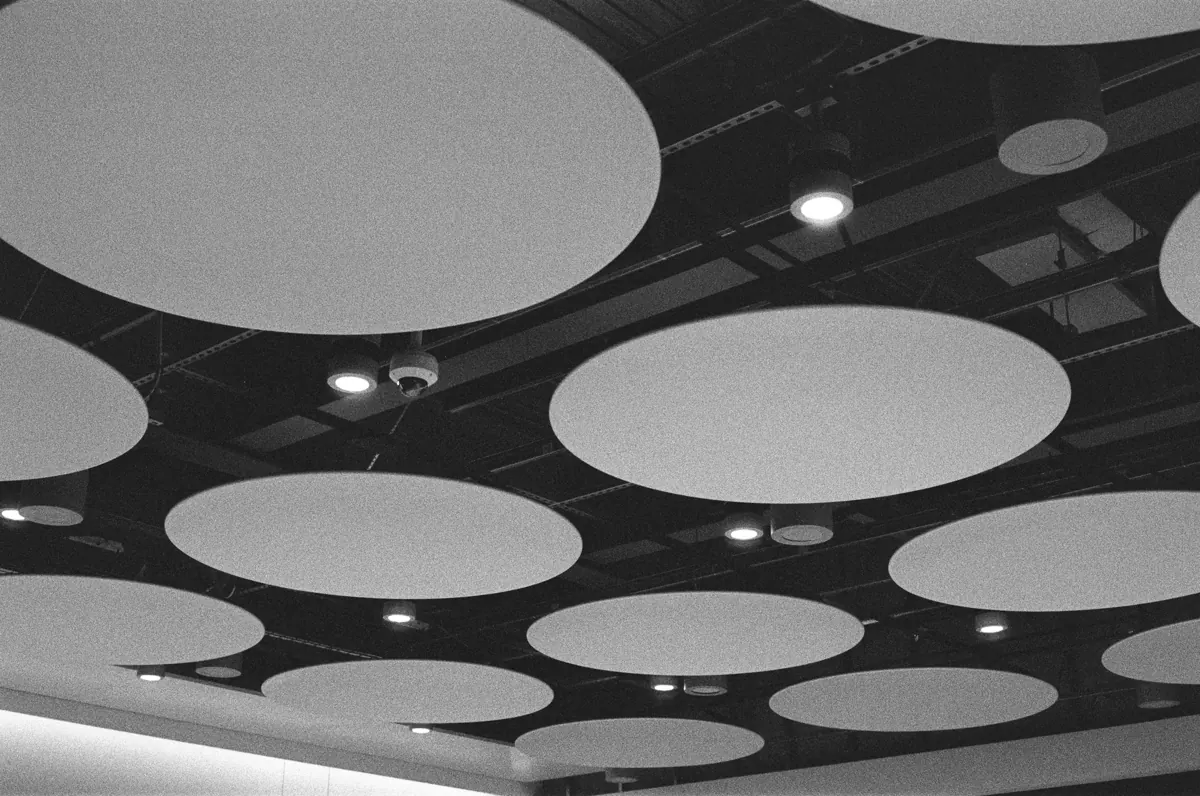 Black-and-white view of round acoustic panels suspended below a dark ceiling with downlights