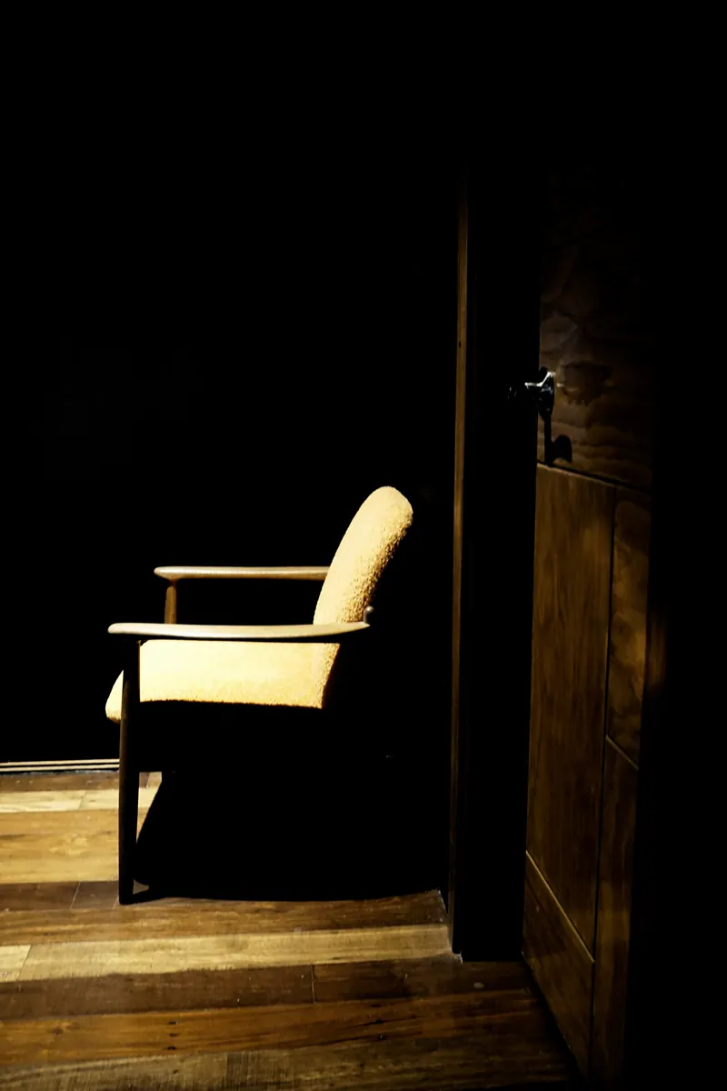 An empty armchair in a dark room, lit by a single shaft of light through a doorway