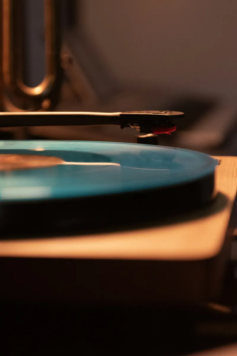 Tonearm and red-tipped cartridge resting over a translucent blue record in warm light