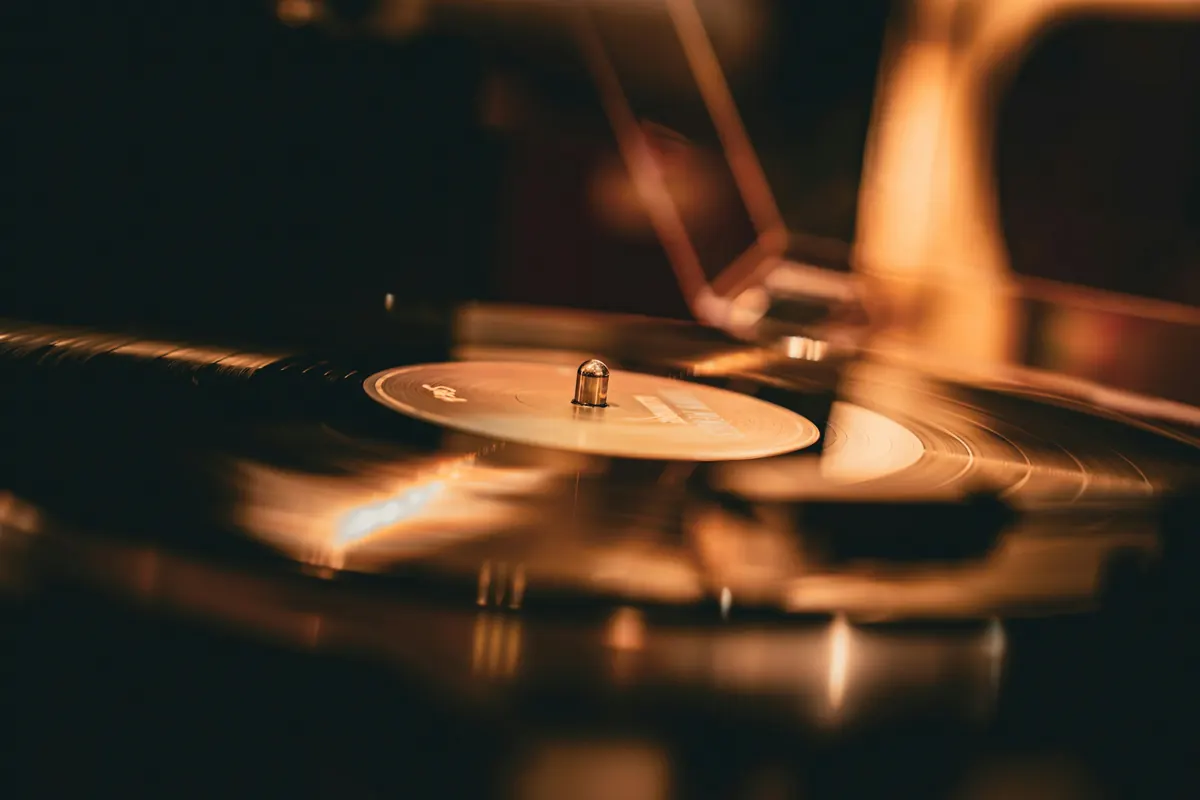Record spinning on a turntable under warm amber light, the tonearm softly out of focus